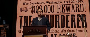 Movie still from “National Treasure: Book of Secrets” (2007), directed by Jon Turteltaub – A man standing at a podium in front of a sign; Medium shot, Over the shoulder angle