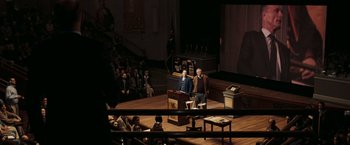 Movie still from “National Treasure: Book of Secrets” (2007), directed by Jon Turteltaub – Two men standing at a podium in front of a crowd; Wide shot, High angle