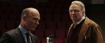 Movie still from “National Treasure: Book of Secrets” (2007), directed by Jon Turteltaub – Two older men standing next to each other in front of a microphone; Medium shot, Over the shoulder angle