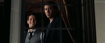 Movie still from “National Treasure: Book of Secrets” (2007), directed by Jon Turteltaub – Two men standing next to each other in front of a window; Medium shot, Low angle