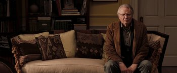 Movie still from “National Treasure: Book of Secrets” (2007), directed by Jon Turteltaub – An older man sitting on a couch in a living room; Medium shot, Over the shoulder angle