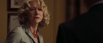 Movie still from “National Treasure: Book of Secrets” (2007), directed by Jon Turteltaub – An older woman with blonde curly hair wearing a red necklace; Close Up shot, Over the shoulder angle