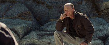 Movie still from “National Treasure: Book of Secrets” (2007), directed by Jon Turteltaub – A man sitting on the ground in front of some rocks; Medium shot, Low angle