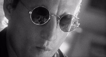 Movie still from “Natural Born Killers” (1994), directed by Oliver Stone – A man wearing a pair of round sunglasses; Extreme Close Up shot, Over the shoulder angle