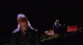 Movie still from “Natural Born Killers” (1994), directed by Oliver Stone – Two people sitting on top of a car at night; Medium shot, Low angle