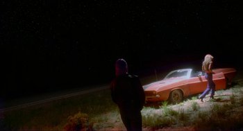 Movie still from “Natural Born Killers” (1994), directed by Oliver Stone – A man standing next to a red car in the dark; Wide shot, Low angle
