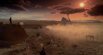 Movie still from “Natural Born Killers” (1994), directed by Oliver Stone – A group of people standing in a field near a mountain; Extreme Wide shot, High angle