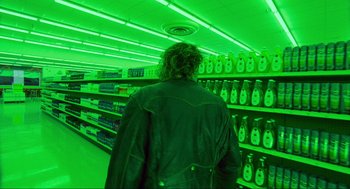 Movie still from “Natural Born Killers” (1994), directed by Oliver Stone – A man in a green lit up aisle of a grocery store; Wide shot, High angle
