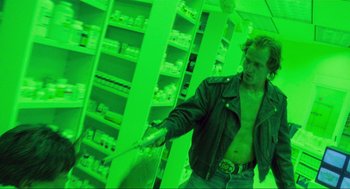 Movie still from “Natural Born Killers” (1994), directed by Oliver Stone – A man holding a baseball bat while standing next to shelves; Medium shot, Over the shoulder angle