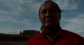 Movie still from “Natural Born Killers” (1994), directed by Oliver Stone – A man in a red shirt is standing in front of a mountain range; Close Up shot, Low angle