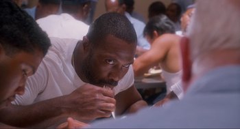Movie still from “Natural Born Killers” (1994), directed by Oliver Stone – A person sitting at a table; Close Up shot, High angle