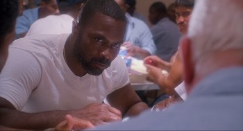Movie still from “Natural Born Killers” (1994), directed by Oliver Stone – A man sitting in front of a group of people; Close Up shot, Over the shoulder angle