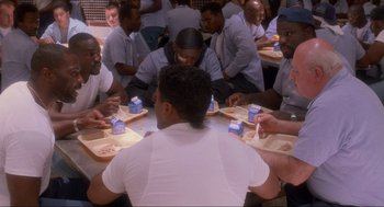 Movie still from “Natural Born Killers” (1994), directed by Oliver Stone – A group of men sitting around a table eating; Wide shot, High angle