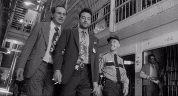 Movie still from “Natural Born Killers” (1994), directed by Oliver Stone – A black - and - white photo of a group of men standing next to each other; Medium shot, Low angle