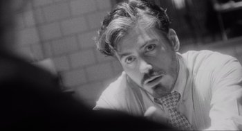 Movie still from “Natural Born Killers” (1994), directed by Oliver Stone – Black and white photograph of a man in a tie looking at the camera; Close Up shot, Over the shoulder angle