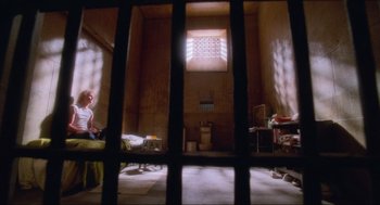 Movie still from “Natural Born Killers” (1994), directed by Oliver Stone – A person sitting in a room with a window and a bed; Extreme Wide shot, High angle