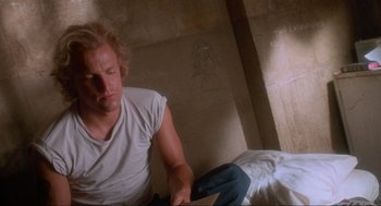 Movie still from “Natural Born Killers” (1994), directed by Oliver Stone – A man sitting on the floor reading a book; Close Up shot, Low angle