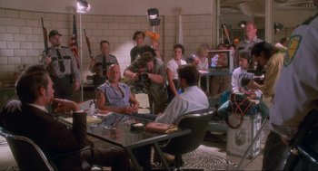 Movie still from “Natural Born Killers” (1994), directed by Oliver Stone – A group of people sitting around a table with a camera; Wide shot, High angle