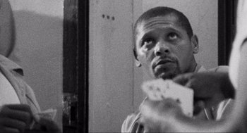 Movie still from “Natural Born Killers” (1994), directed by Oliver Stone – A black and white photo of a man holding a pair of playing cards; Close Up shot, Low angle