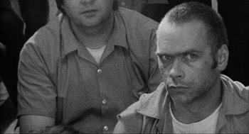 Movie still from “Natural Born Killers” (1994), directed by Oliver Stone – Two men sitting next to each other in front of a wall; Close Up shot, Over the shoulder angle