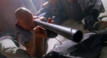Movie still from “Natural Born Killers” (1994), directed by Oliver Stone – A man is holding a rifle in a room; Medium shot, Low angle