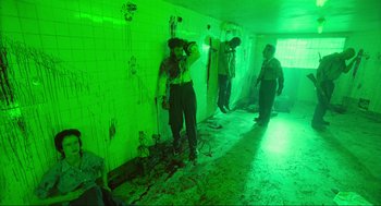Movie still from “Natural Born Killers” (1994), directed by Oliver Stone – A group of people standing in a room with green lighting; Wide shot, High angle