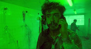 Movie still from “Natural Born Killers” (1994), directed by Oliver Stone – A man in a green room talking on a cell phone; Close Up shot, Low angle