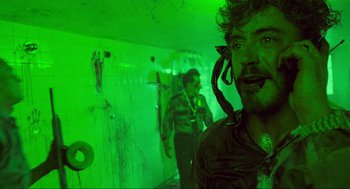 Movie still from “Natural Born Killers” (1994), directed by Oliver Stone – A man in a green room with two other men in the background; Medium shot, Over the shoulder angle