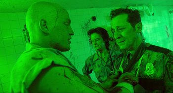 Movie still from “Natural Born Killers” (1994), directed by Oliver Stone – A group of people standing next to each other in a room; Medium shot, Over the shoulder angle