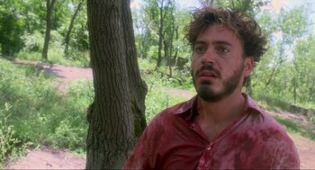 Movie still from “Natural Born Killers” (1994), directed by Oliver Stone – A man in a red shirt is standing by a tree; Close Up shot, Over the shoulder angle