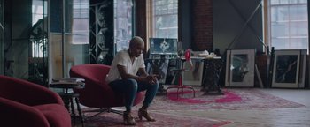 Movie still from “Needle in a Timestack” (2021), directed by John Ridley – A woman sitting on a chair in a room; Wide shot, Low angle