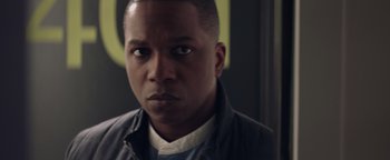Movie still from “Needle in a Timestack” (2021), directed by John Ridley – A person wearing a jacket looking at the camera; Close Up shot, Over the shoulder angle