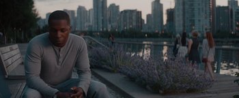 Movie still from “Needle in a Timestack” (2021), directed by John Ridley – A man sitting on the side of a river next to flowers; Medium shot, Low angle