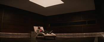 Movie still from “Needle in a Timestack” (2021), directed by John Ridley – A man sitting on a chair in a room; Wide shot, High angle
