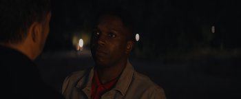 Movie still from “Needle in a Timestack” (2021), directed by John Ridley – A man in a red shirt is looking at the camera; Close Up shot, Low angle