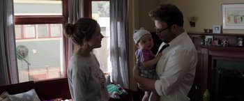 Movie still from “Neighbors” (2014), directed by Nicholas Stoller – A man and woman holding a baby in front of a window; Medium shot, Over the shoulder angle
