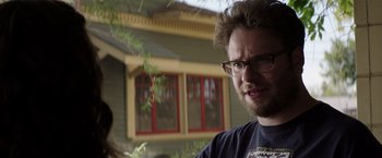 Movie still from “Neighbors” (2014), directed by Nicholas Stoller – A person wearing glasses near a building; Close Up shot, Over the shoulder angle