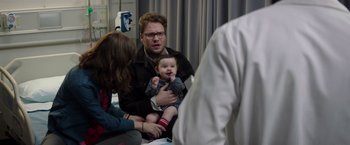 Movie still from “Neighbors” (2014), directed by Nicholas Stoller – A man holding a baby in his arms while sitting next to a woman; Medium shot, Over the shoulder angle