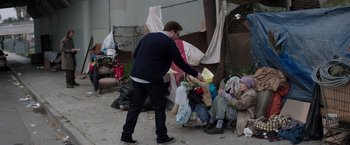 Movie still from “Neighbors” (2014), directed by Nicholas Stoller – A man is handing something to a homeless person; Wide shot, Over the shoulder angle