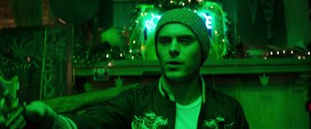 Movie still from “Neighbors” (2014), directed by Nicholas Stoller – A man in a beanie and jacket in front of neon lights; Close Up shot, Low angle
