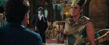 Movie still from “Night at the Museum: Battle of the Smithsonian” (2009), directed by Shawn Levy – A man dressed as a pharaoh holding a hourglass in front of another man in a suit and tie; Medium shot, Over the shoulder angle