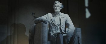 Movie still from “Night at the Museum: Battle of the Smithsonian” (2009), directed by Shawn Levy – A statue of abraham lincoln sitting on top of a wooden post; Medium shot, Low angle