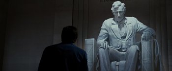 Movie still from “Night at the Museum: Battle of the Smithsonian” (2009), directed by Shawn Levy – A man standing in front of a large statue of a man; Medium shot, Over the shoulder angle