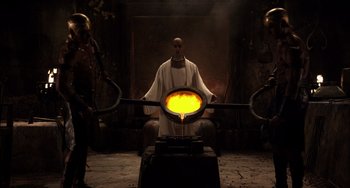 Movie still from “Night at the Museum: Secret of the Tomb” (2014), directed by Shawn Levy – A man in a white robe is casting a golden object into a furnace; Medium shot, Low angle