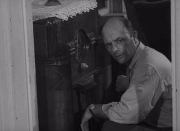 Movie still from “Night of the Living Dead” (1968), directed by George A. Romero – A man leaning against a fire hydrant in a room; Medium shot, Low angle