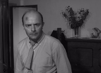 Movie still from “Night of the Living Dead” (1968), directed by George A. Romero – A man in a shirt and tie standing next to a table; Close Up shot, Low angle