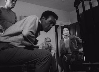 Movie still from “Night of the Living Dead” (1968), directed by George A. Romero – A group of men and women sitting in a living room; Medium shot, High angle