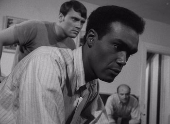 Movie still from “Night of the Living Dead” (1968), directed by George A. Romero – A man in a striped dress shirt is looking at the camera while two other men look on; Close Up shot, Low angle