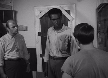 Movie still from “Night of the Living Dead” (1968), directed by George A. Romero – A man standing in front of two other men; Medium shot, Over the shoulder angle