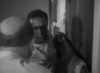 Movie still from “Night of the Living Dead” (1968), directed by George A. Romero – A black and white photo of a man leaning against a wall; Close Up shot, Over the shoulder angle